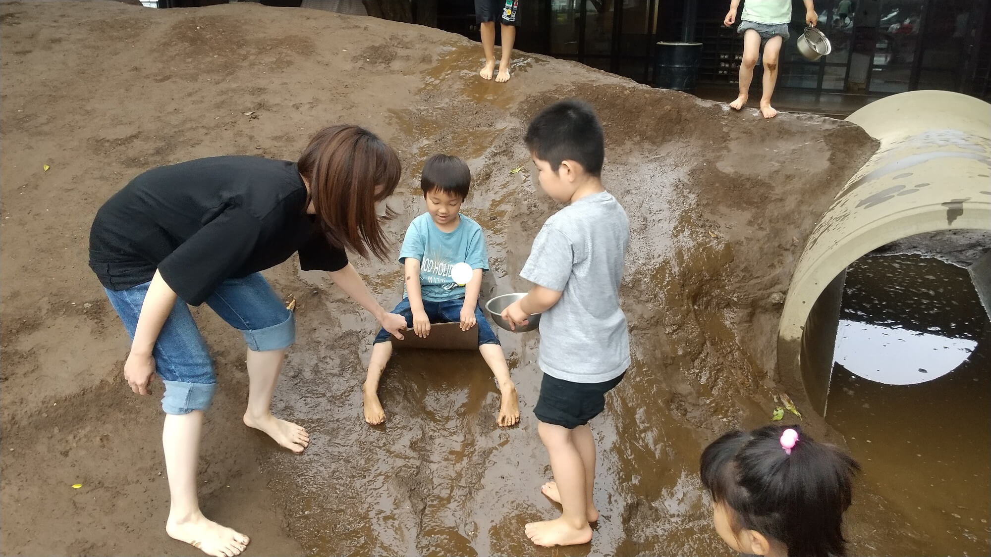 ドロドロの斜面を滑って遊ぶ子ども