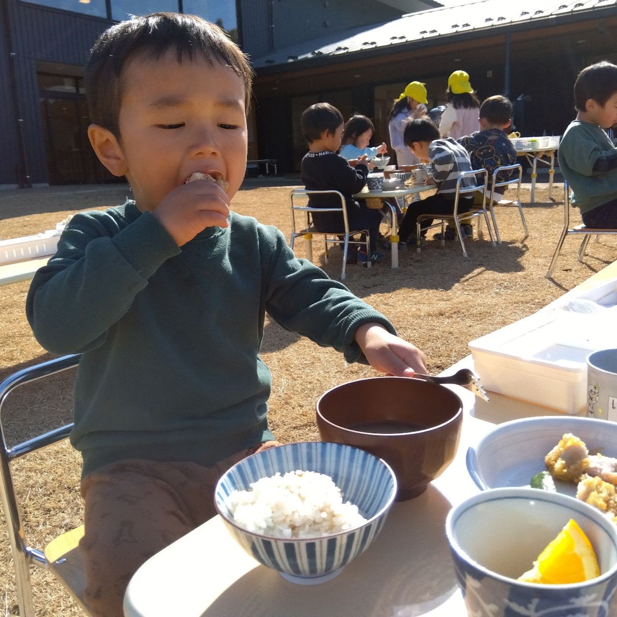 園庭にテーブルを出して昼食をとる子どもたち