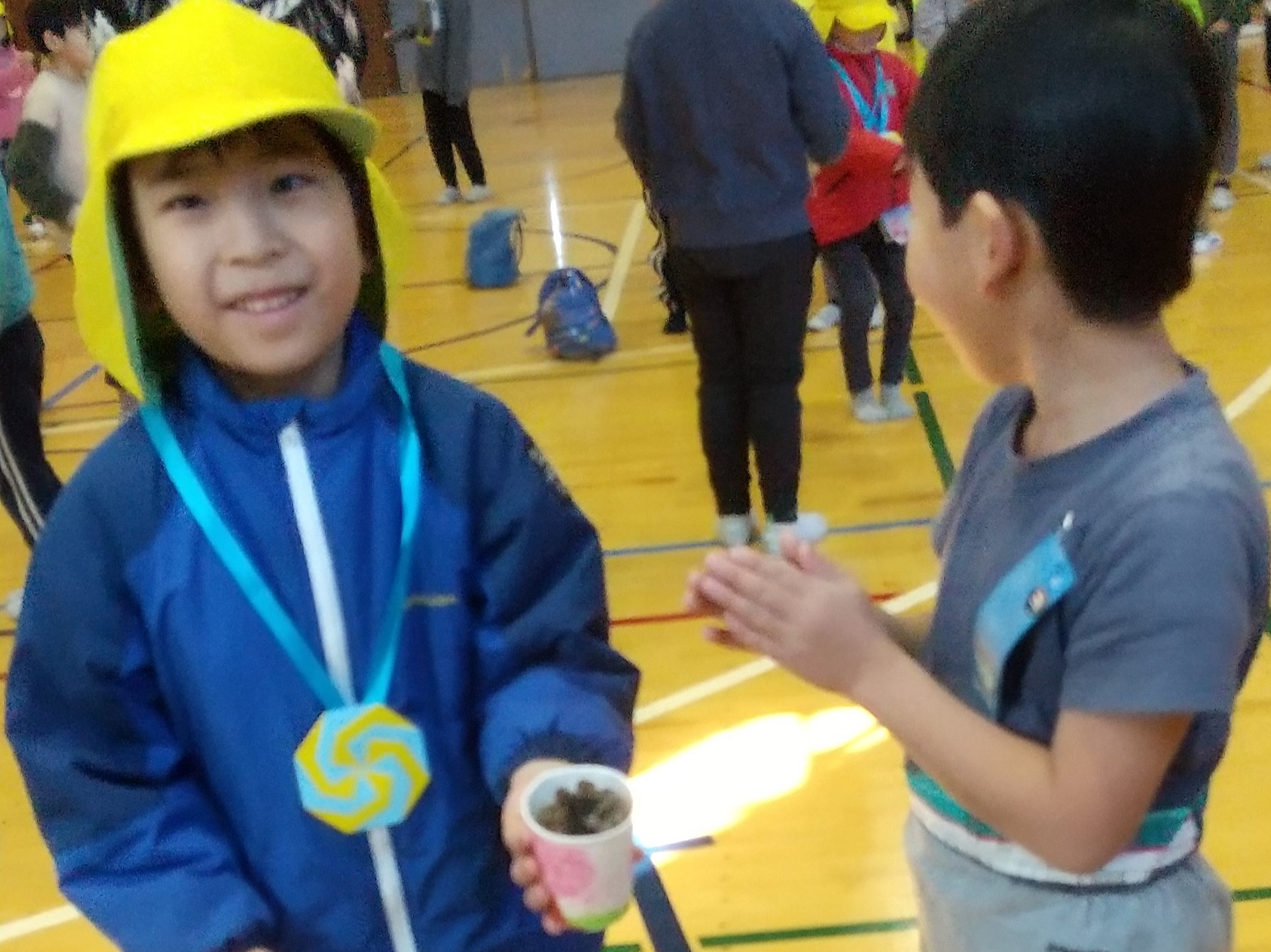 小学校の体育館で、松ぼっくりのけん玉で遊ぶ子どもたち