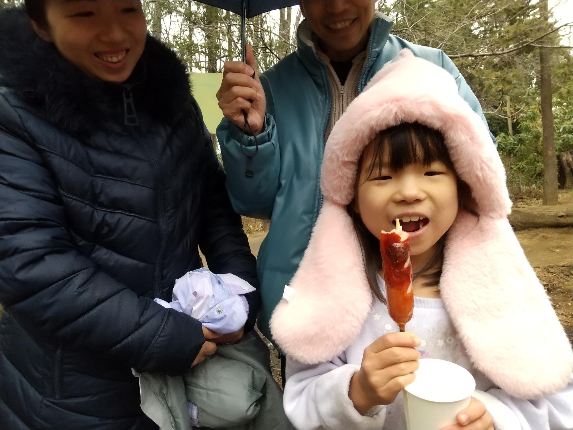 焚き火で作ったフランクフルトを食べる子どもと見守る保護者