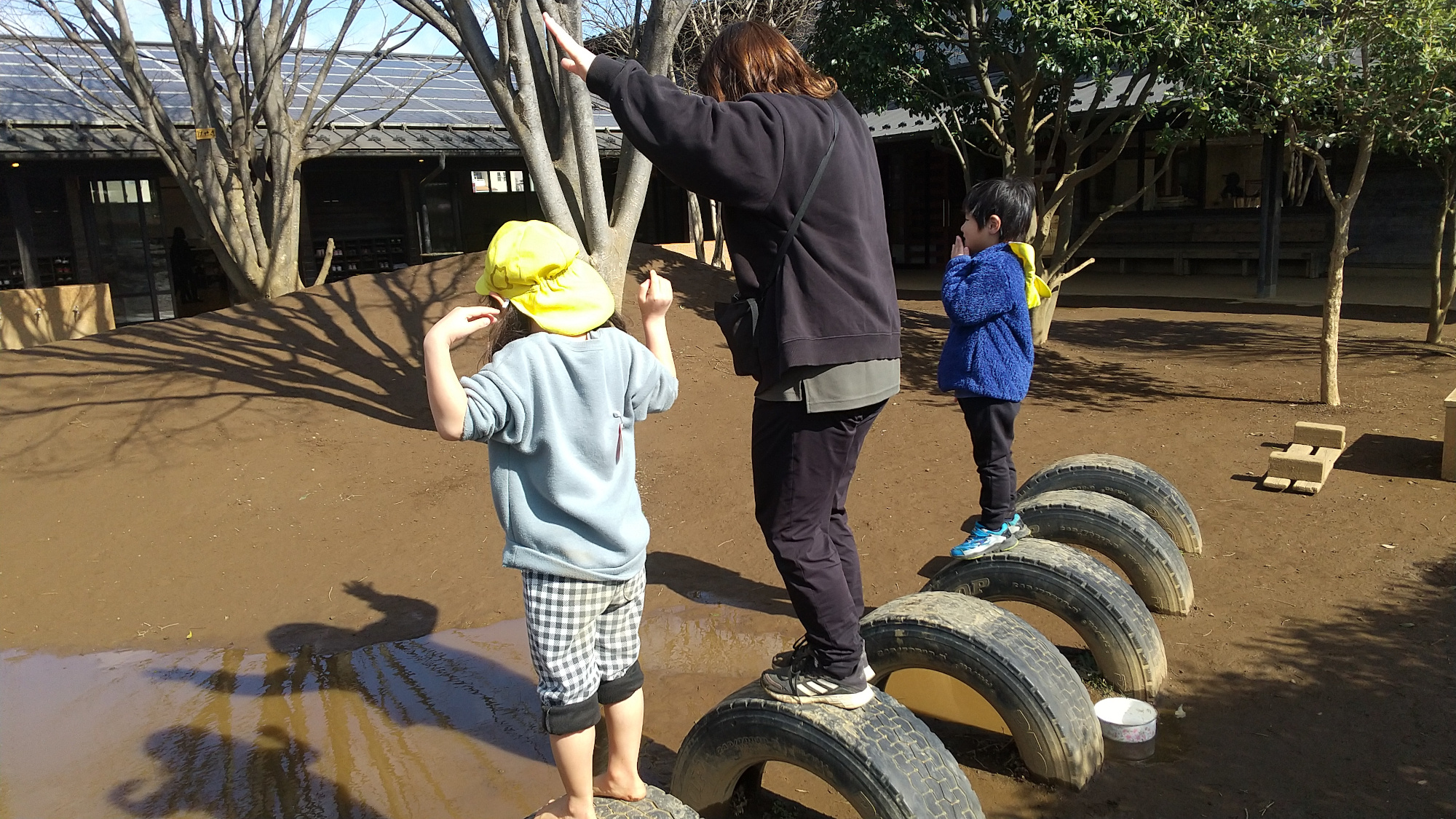 園庭で、水たまりに写る自分の姿を見て楽しむ子どもとスタッフ