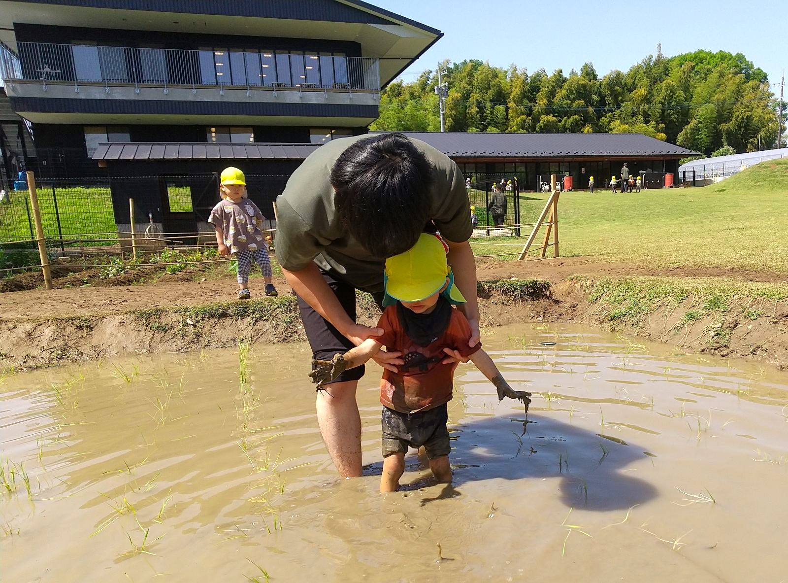 スタッフに支えられながら田んぼに足を踏み入れる子ども