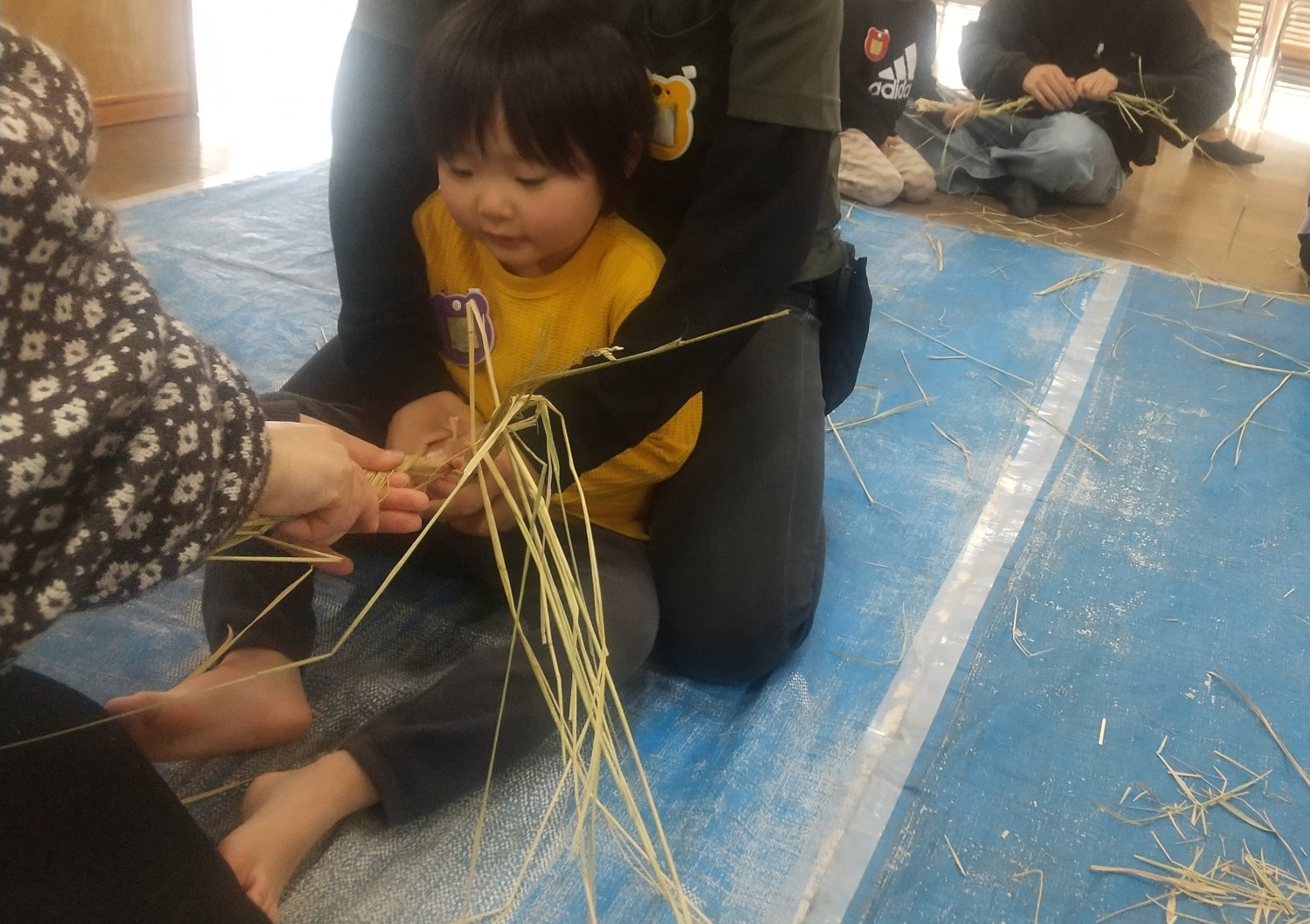 大人の力を借りながら藁をねじる子ども