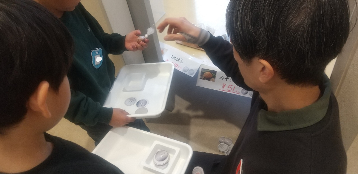 自作のお金でおにぎりの具を購入する子どもたち