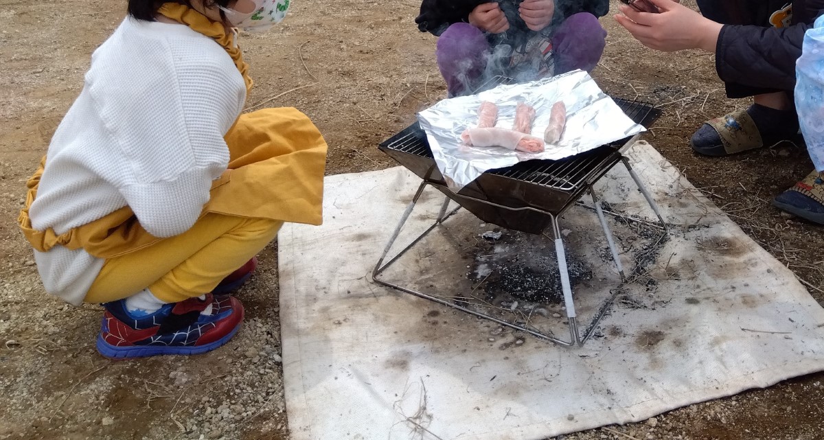 焚き火でソーセージを焼く子どもたち