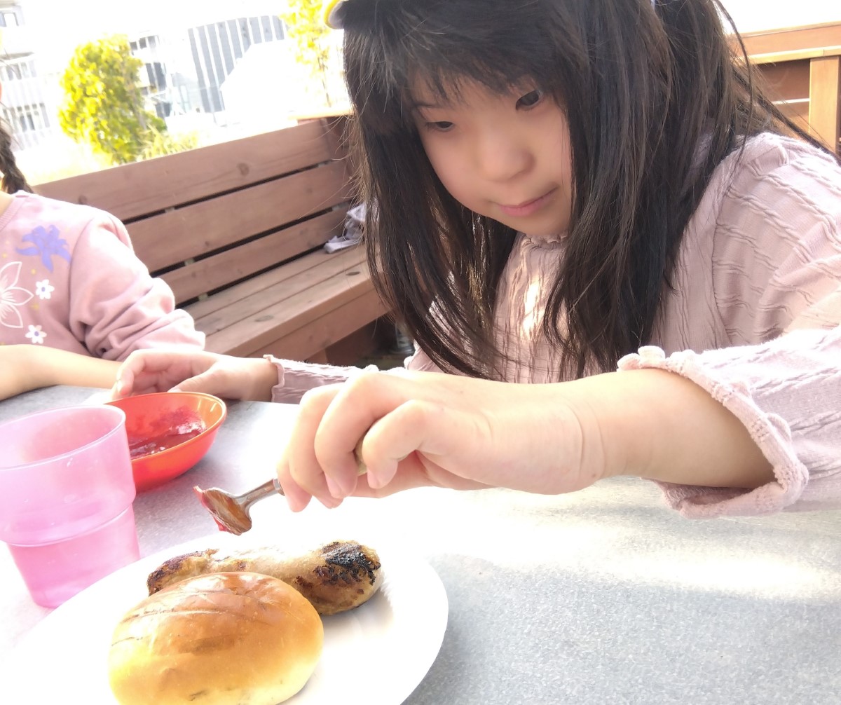 焼けたソーセージにケチャップを塗る子ども