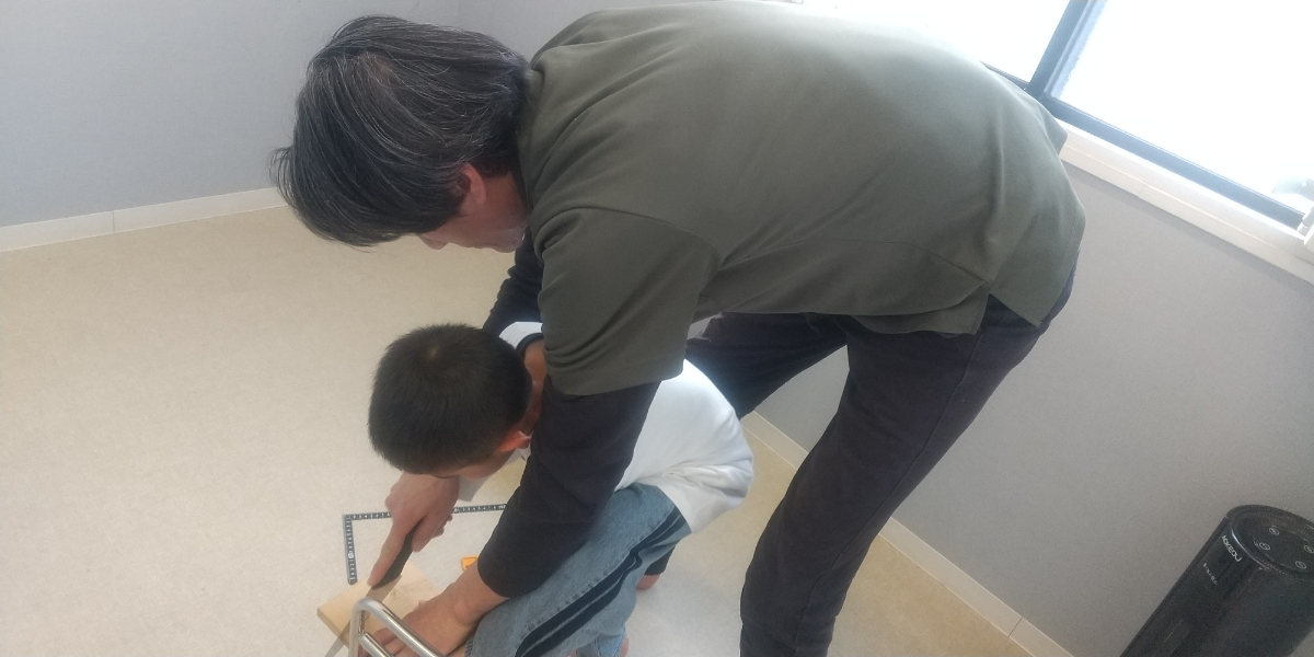 保育者と一緒にノコギリを使う子ども