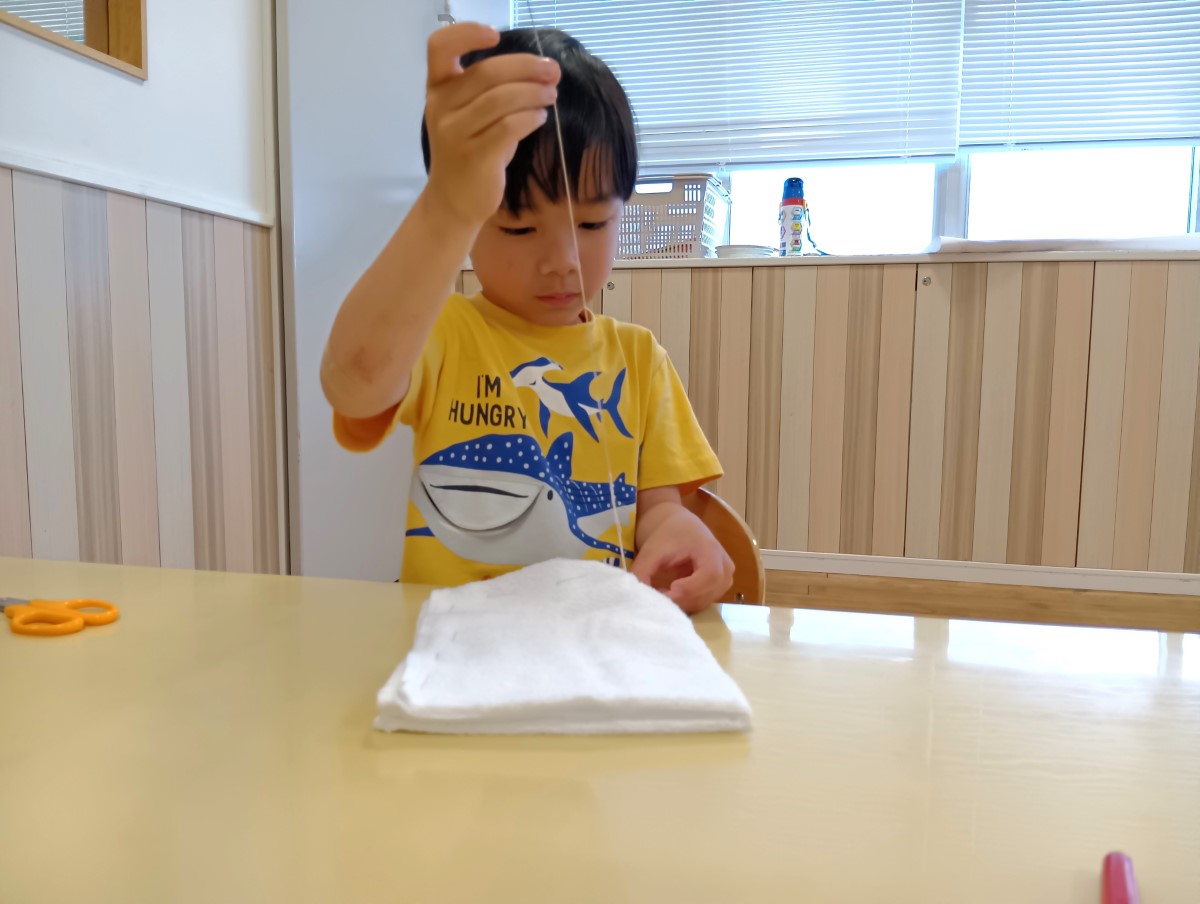 針と糸で雑巾を縫う子ども