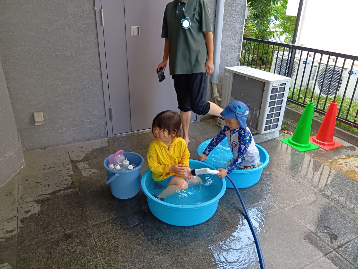 タライに水を溜めて水遊びをする子どもたち