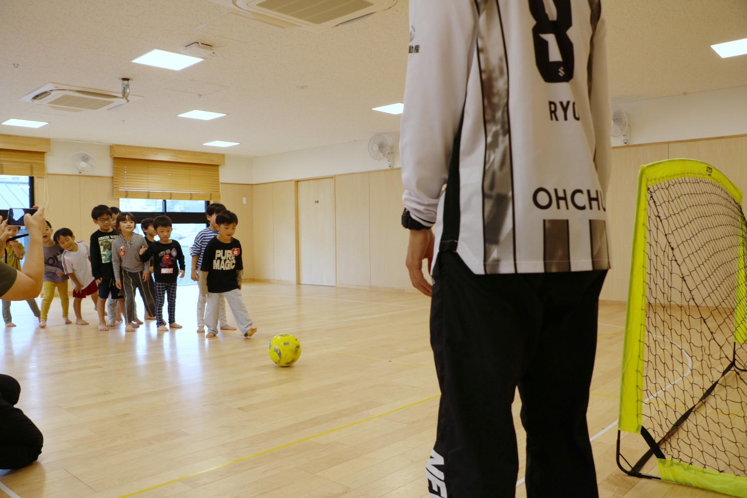 みんなに見守られながら、ゴールに向かってボールを蹴る子ども