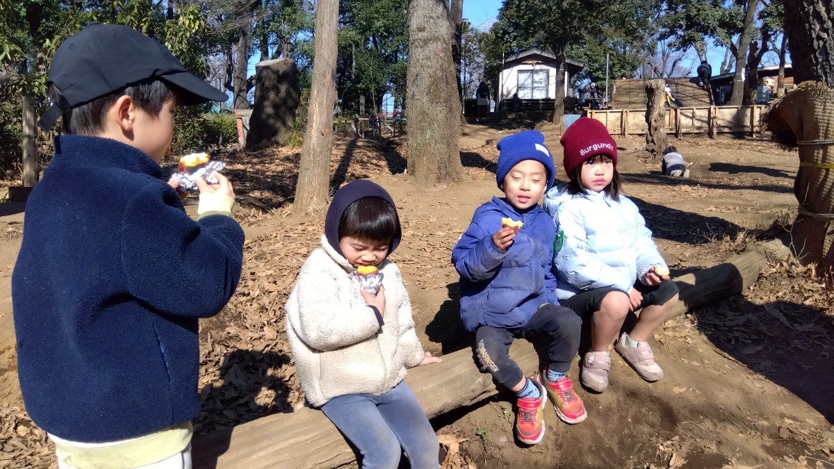 並んで座って焼き芋を食べる子どもたち