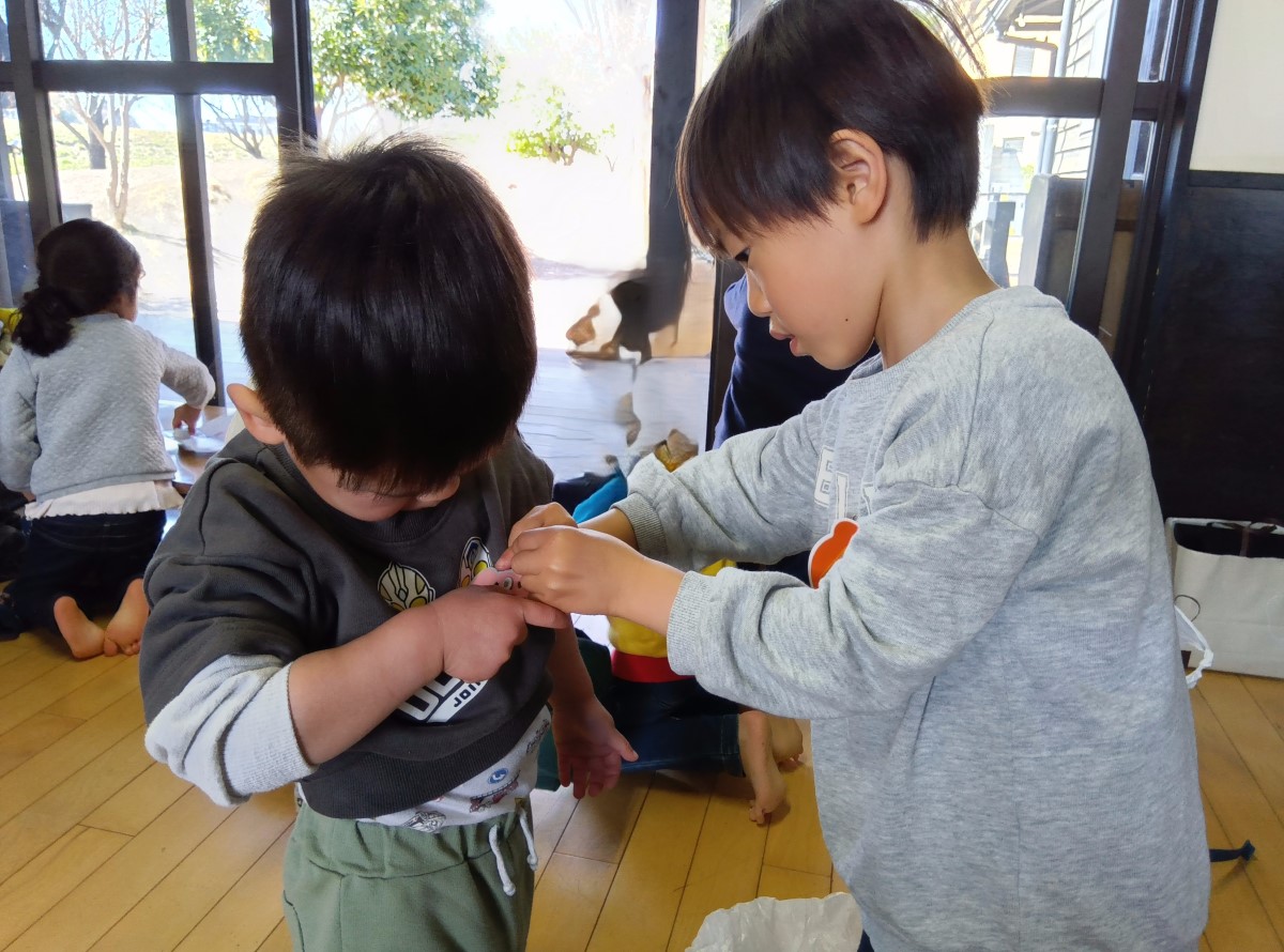 年下の子に名札を付けてあげる子どもの様子