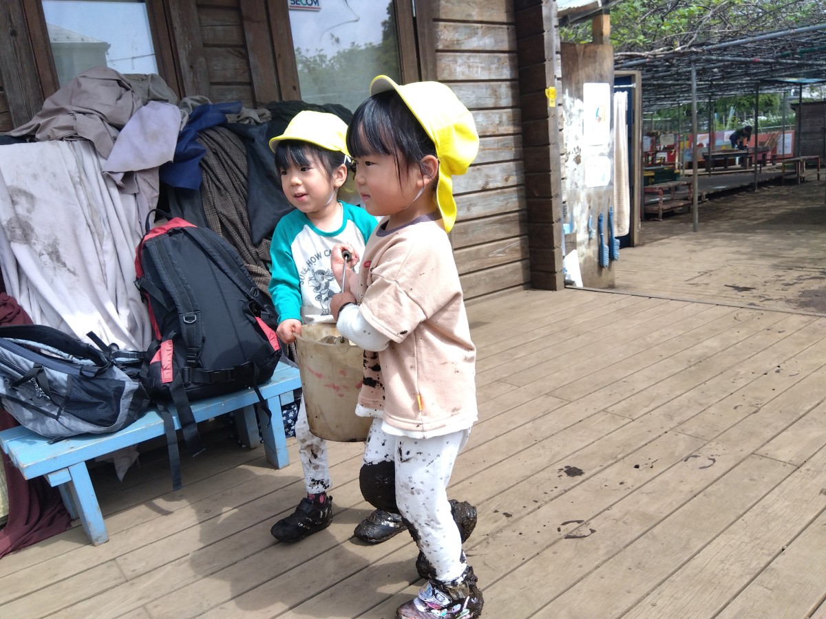 2人のこどもが、水の入った一つのバケツを協力して持ち運んでいる