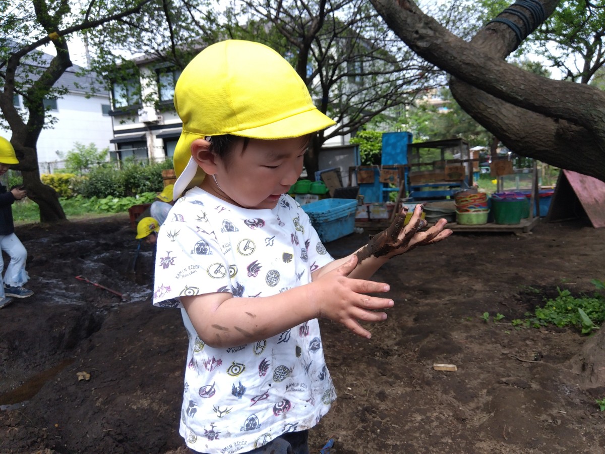 子どもが自らの手についた泥を見つめ、指で触り感触を確かめている