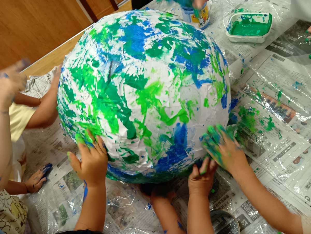 子どもたちは手や指先を使い、紙が貼られた球体に緑や青の絵の具で色を付けている