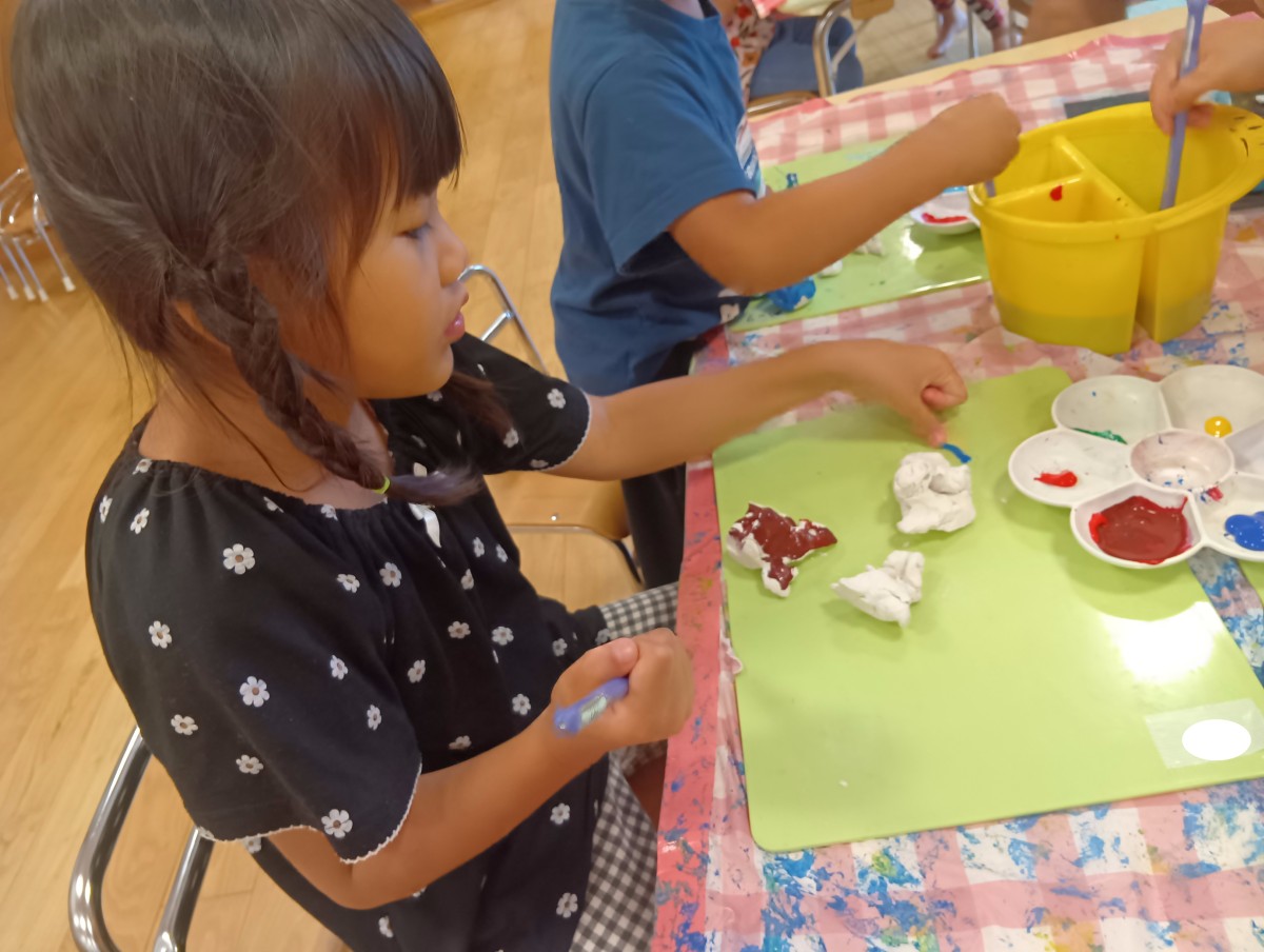 子どもたちは筆と絵の具を使い紙粘土の作品に色付けをしている