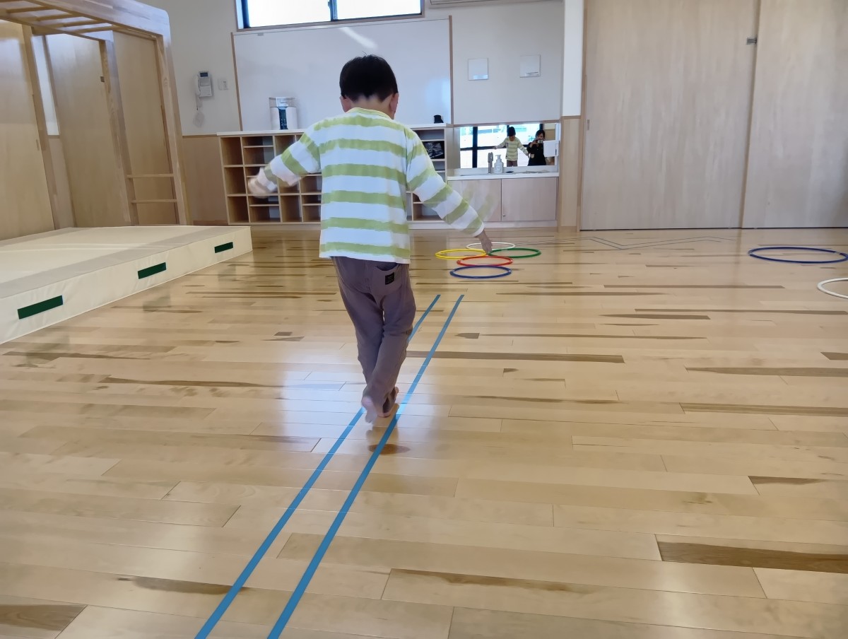 床にはビニールテープで2本の線が貼ってあり、その間を一人の子どもが足元を見ながら歩いている