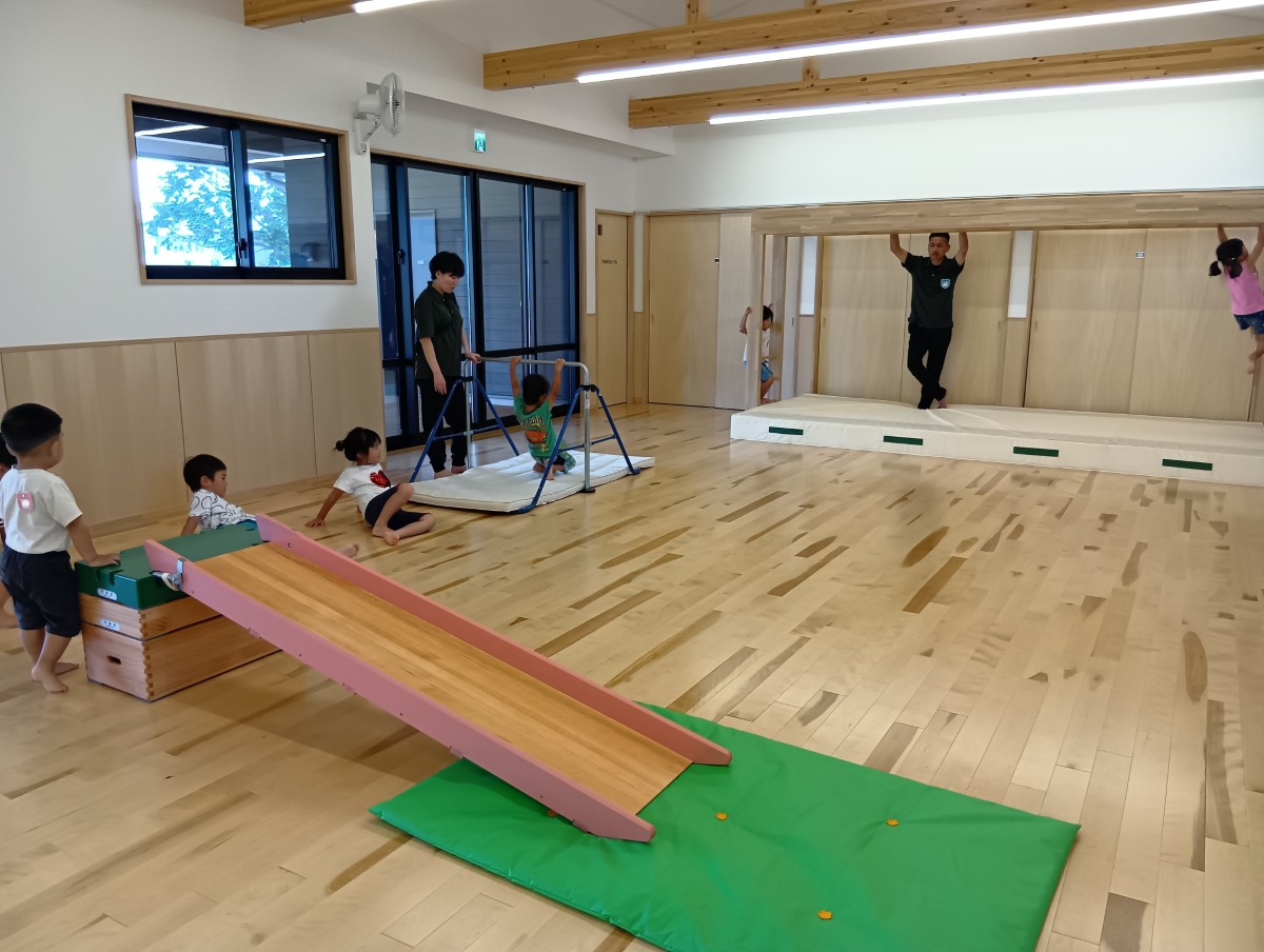 室内では、滑り台、鉄棒、雲梯がサーキット形式で置かれており、子どもたちは順番に並んで鉄棒や雲梯でぶら下がったり自分の番を待ったりしている