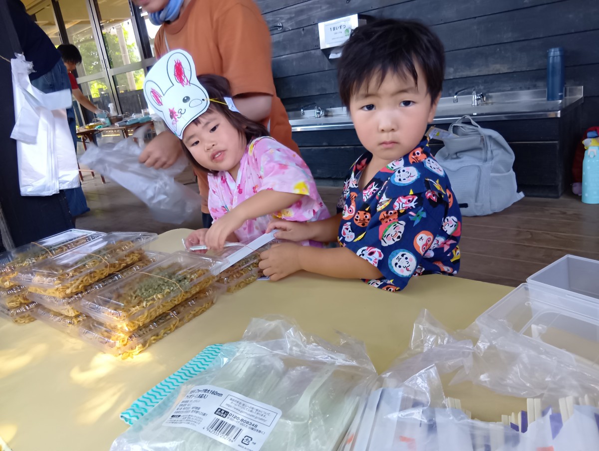 甚平を着た二人の子どもが、焼きそばコーナーで店番をしている