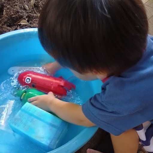 一人の子どもが水が入ったたらいの中の手作り玩具に手を伸ばしている