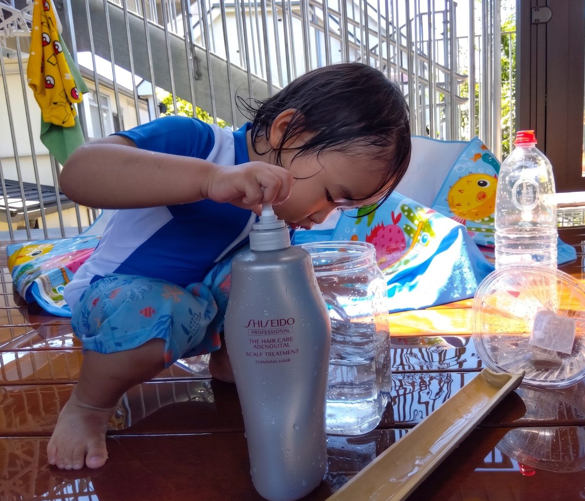 テラスでは、水着を着た子どもが水が入った大きいペットボトルの中を覗き込んでいる