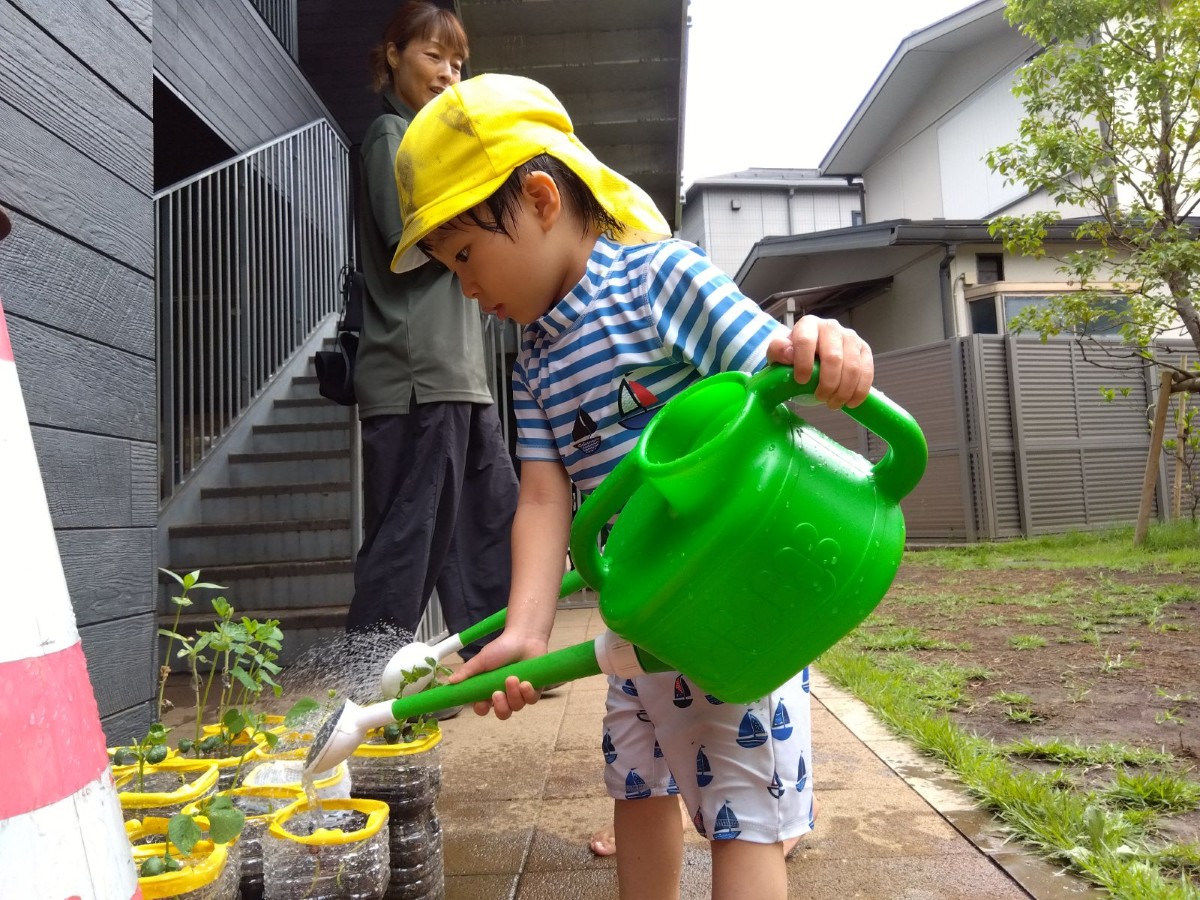 水着を着た子どもが、じょうろを持って植物に水をあげている
