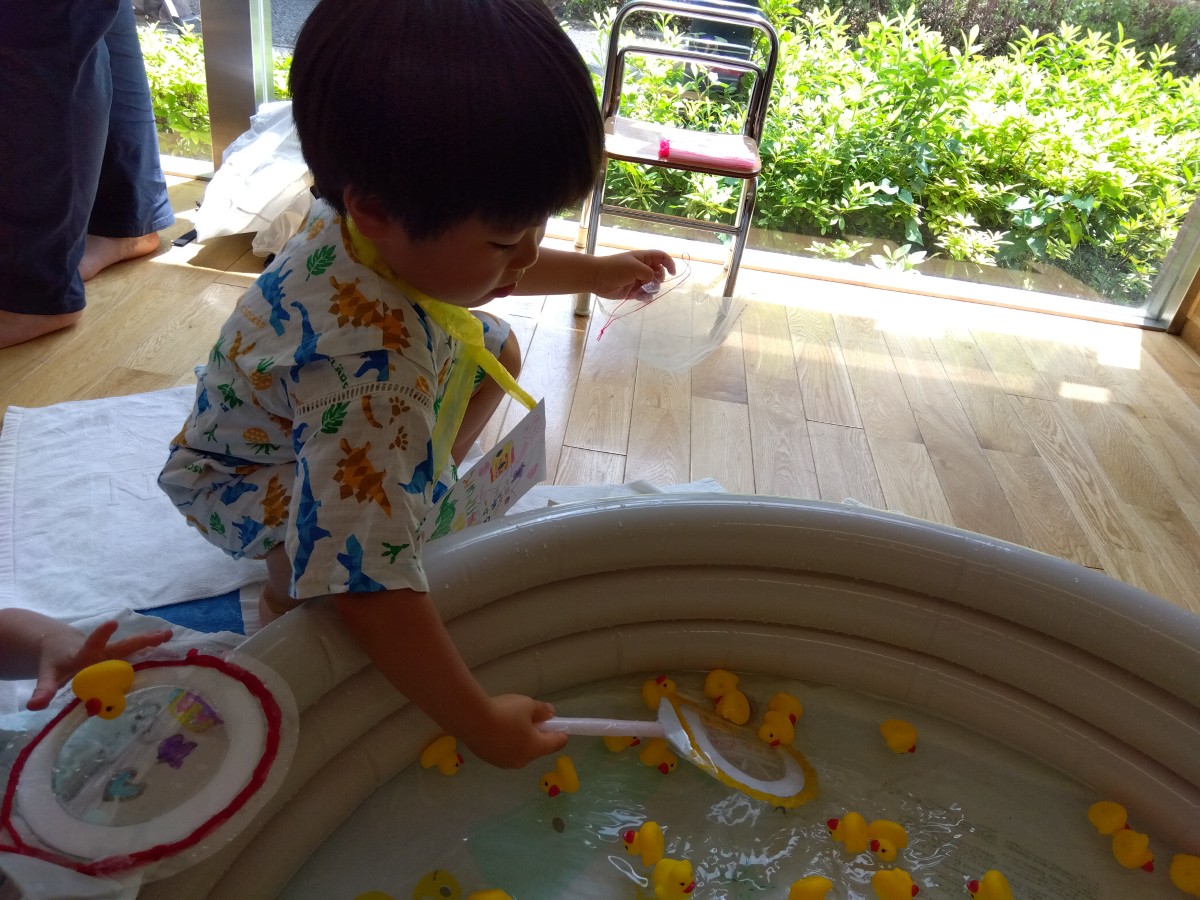 ビニールプールの中にたくさんのアヒルの人形が浮いており、子どもたちは手作りの網でアヒルの人形をすくっている