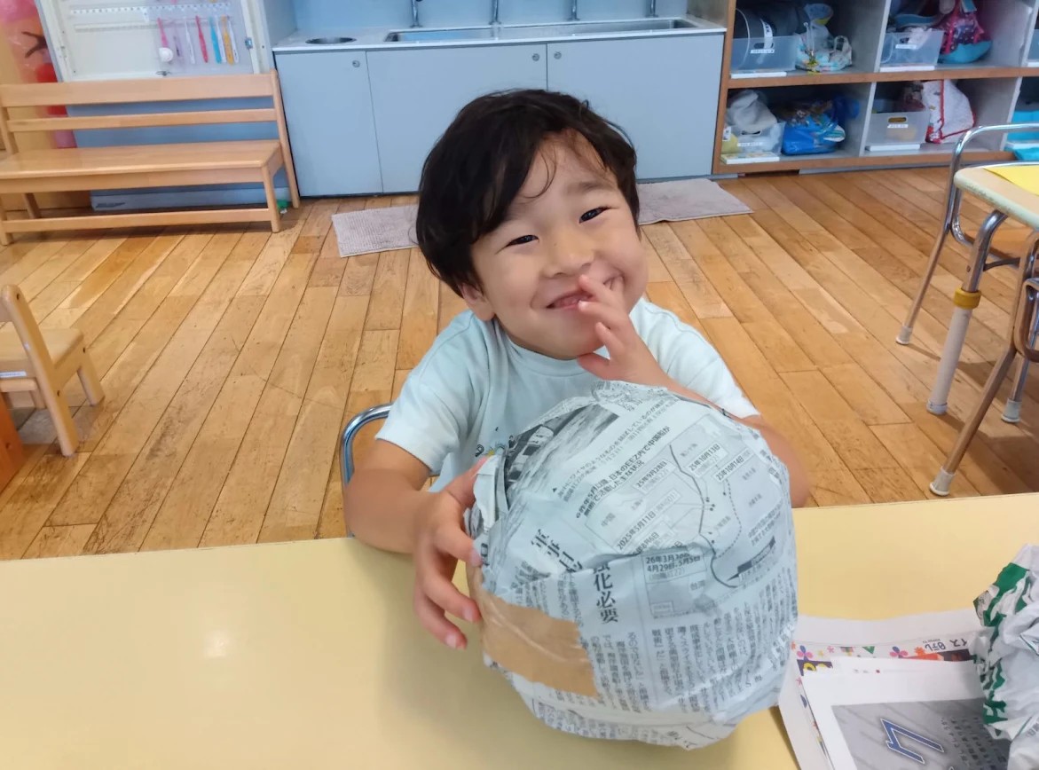 一人の子どもが、丸められた新聞紙に手を添えて笑っている