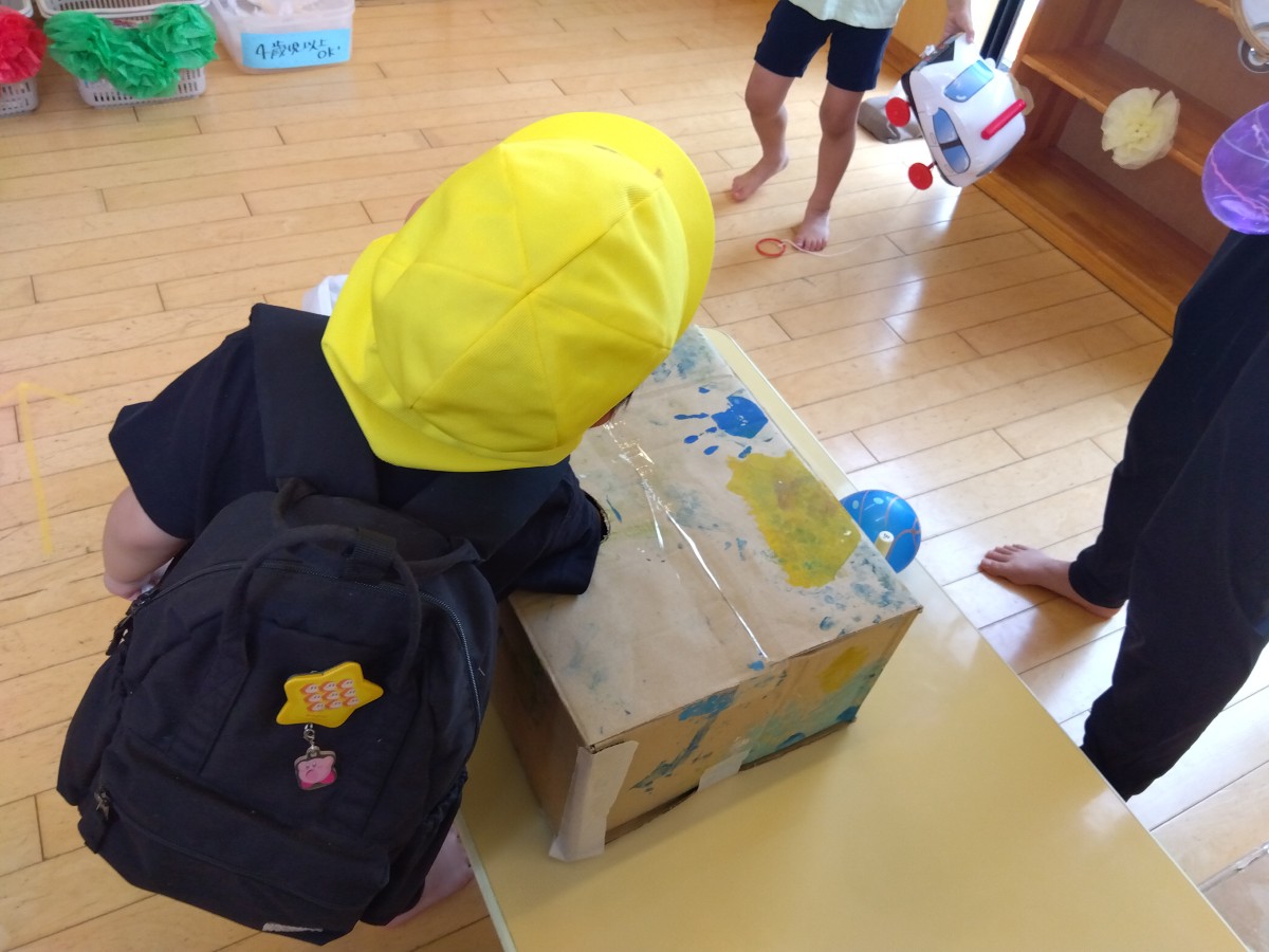 一人の子どもが穴の空いた段ボールに腕を入れている