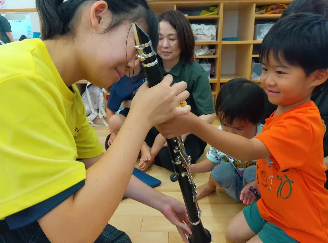 一人の子どもが中学生が持っているクラリネットのキイに子どもが触れている