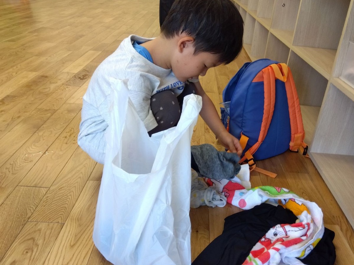 一人の子どもがビニール袋と衣服やタオルを目の前にしてしゃがんでいる