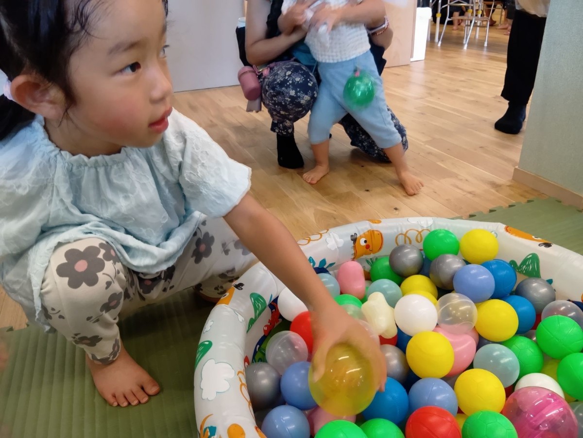 カラーボールが入ったビニールプールの傍に子どもが座り、一つのボールを手に取っている