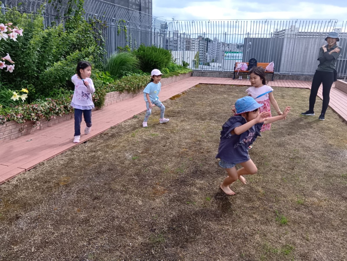 テラスで子どもたちが走り回っており、近くで一人の大人が笑顔で見守っている