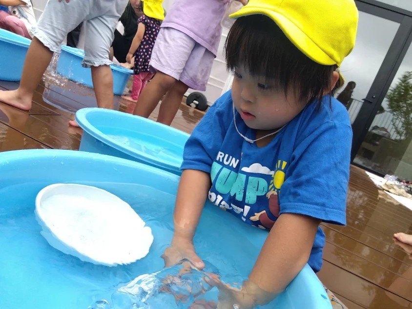 一人の子どもが、たらいの中の水の中にペットボトルを沈めながら手を入れている。
