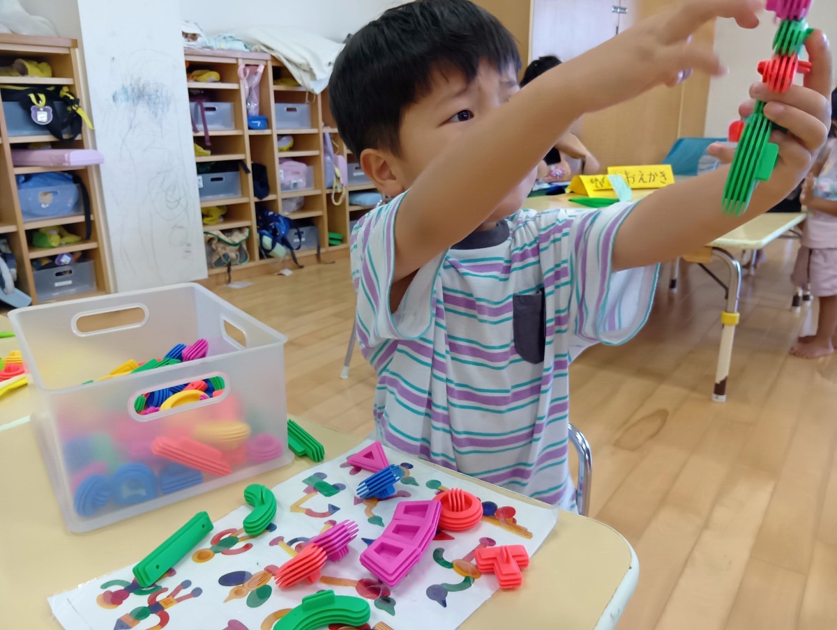 シリコンブロックが置かれた机には、一人の子どもが手本の上にブロックを広げつながったブロックの一部を指さしている