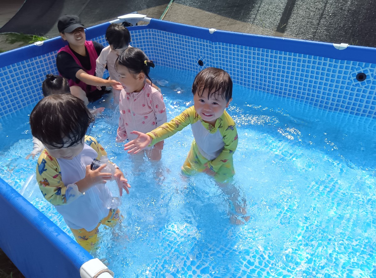 プールでは、一人の子どもが友達に笑顔で水をかけている