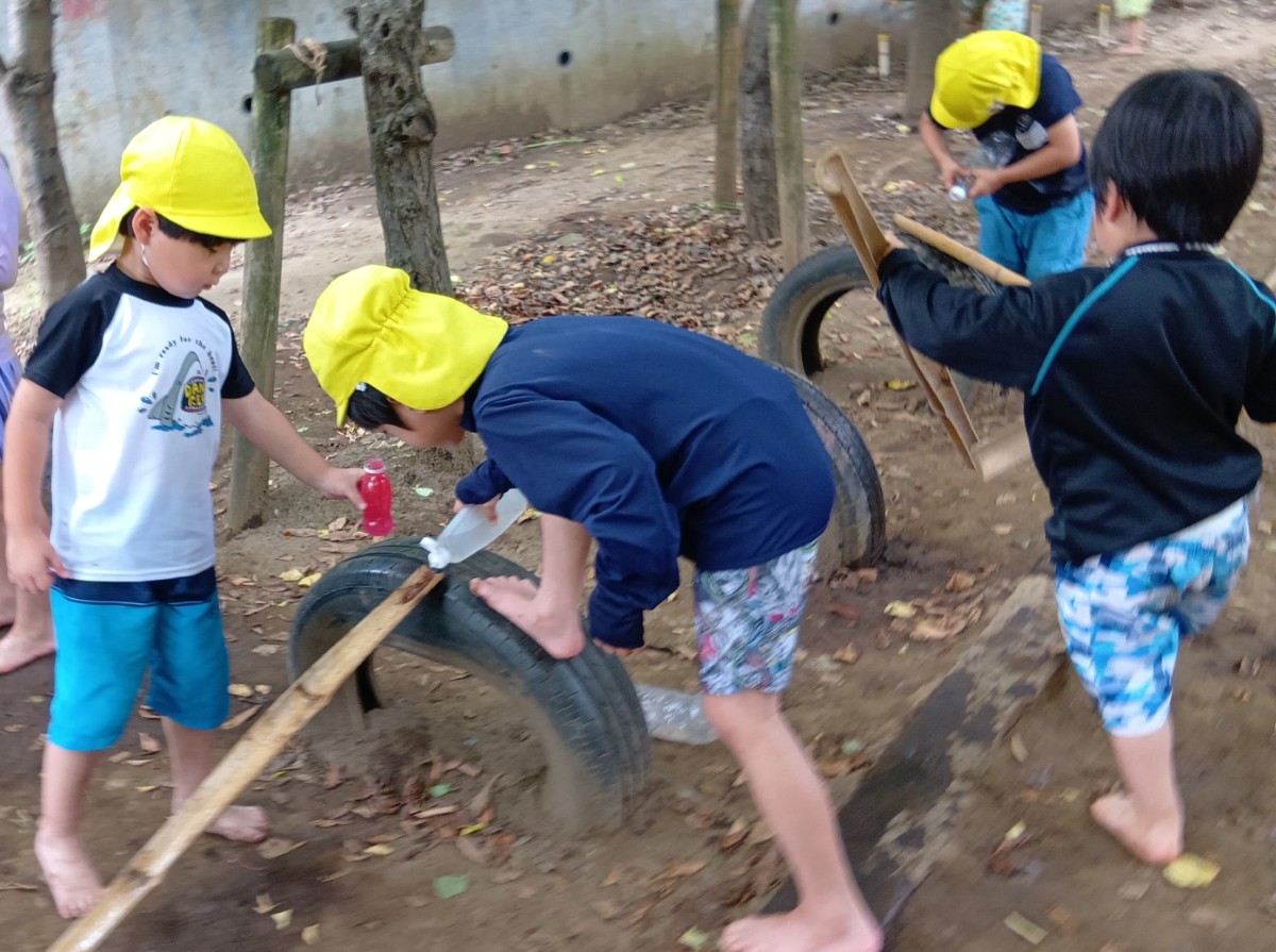 園庭のタイヤの上で、子どもたちはそれぞれでタイヤに立て掛けた竹に水や色水を流している