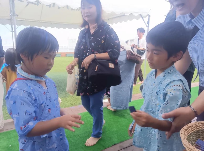 チケットを持った子どもの後ろには大人が子どもの腕を支えており、向かい合っている一人の子どもは手を伸ばそうとしている