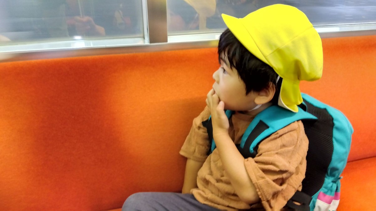一人の子どもが電車の席に座り、窓の外を見ている