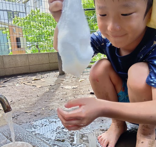一人の子どもが、水を含んだ綿を片手で持ち上げ、反対の手は綿の下から垂れる水に触れて感触を味わっている