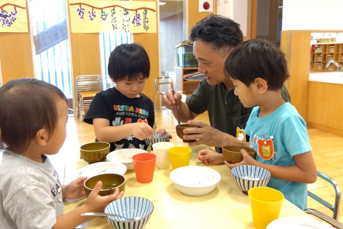 一人の大人と子どもたちは同じ机で給食を食べている
