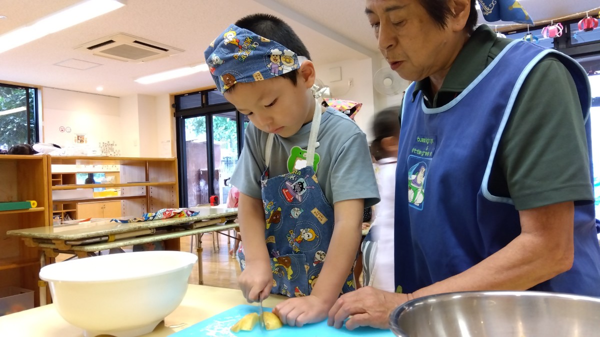 エプロン三角巾を着けた子どもが包丁でジャガイモを切っている
