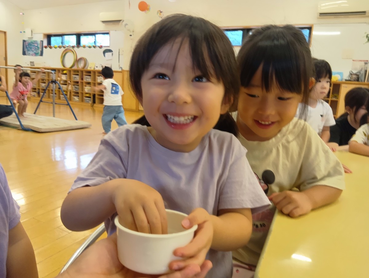 一人の子どもがカップに手を入れて笑っており、後ろにいる友達はカップの中をのぞいて笑っている