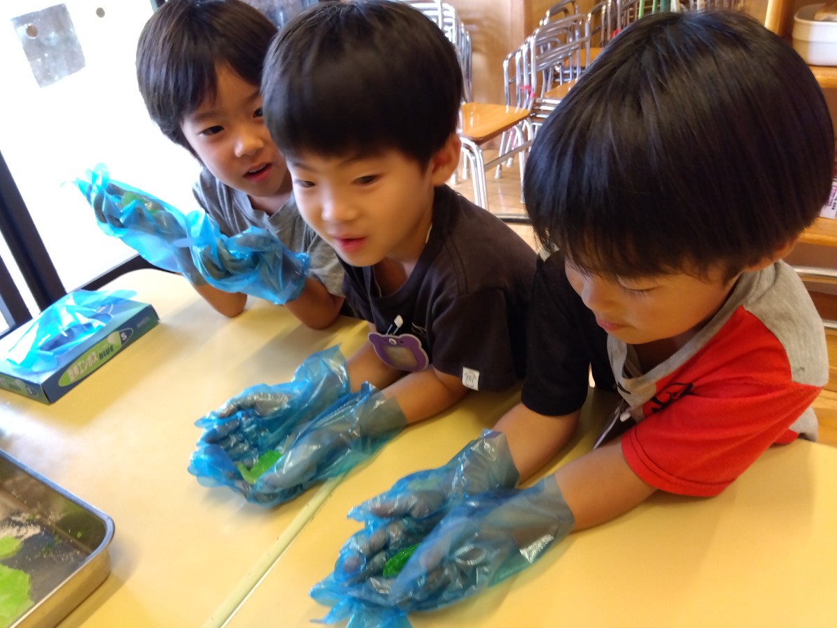 3人の子どもがビニール手袋をはめて、緑色のゼリーを両手に持っている