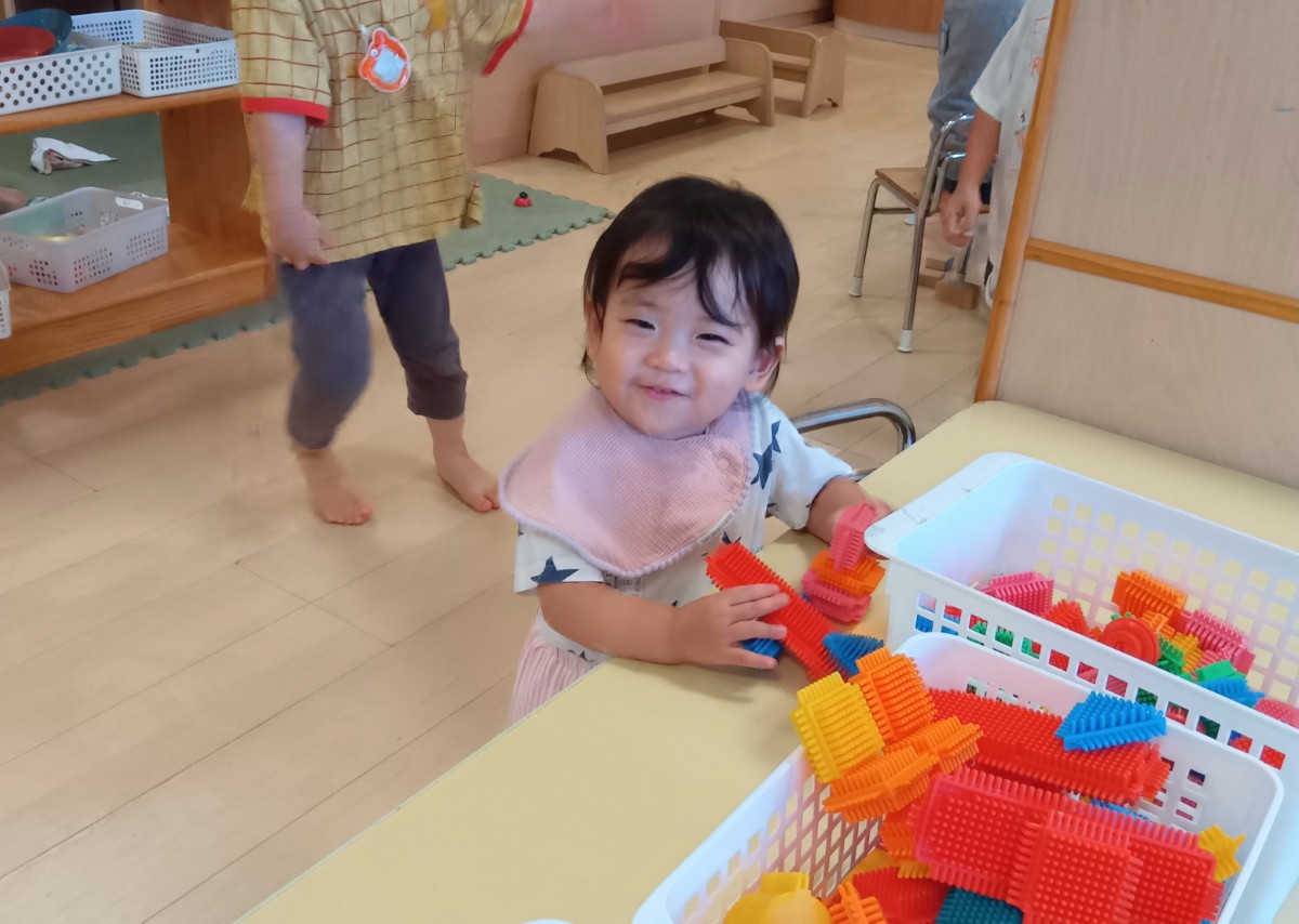 室内では、子どもがソフトブロックを両手に持ち笑顔を見せている