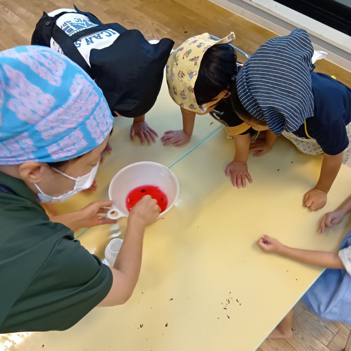 桃紫色の液体が入った皿の中を子どもたちが覗き込んでいる