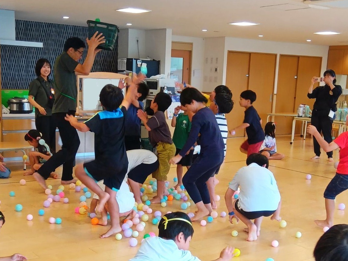 室内では一人の大人が籠を持って立ち、子どもたちはカラーボールを籠をめがけて投げ入れている