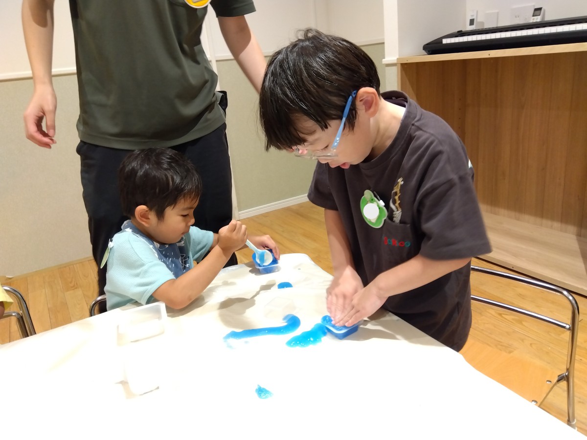 子どもたちは、スプーンや手を使ってスライムを容器に入れている
