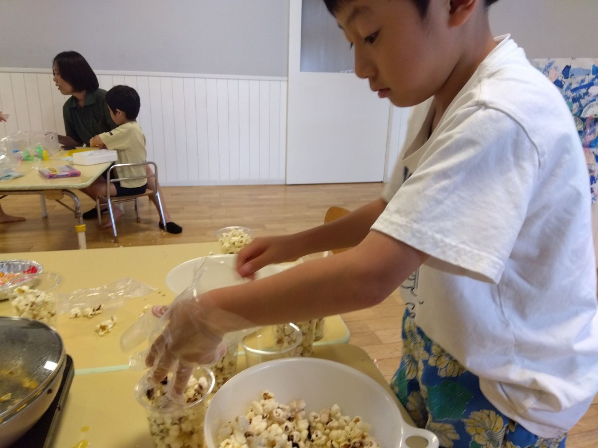 一人の子どもが、ビニール手袋を手にはめて出来上がったポップコーンを透明カップに入れている