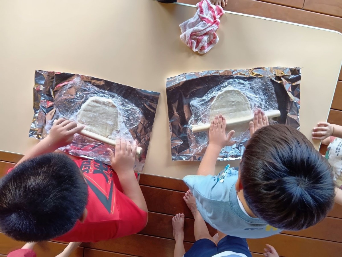 アルミホイルの上に生地を置き、二人の子どもが麺棒で生地を伸ばしている